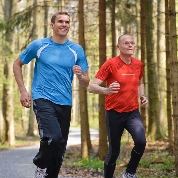 Mann joggt mit Personal Trainer im Wald
